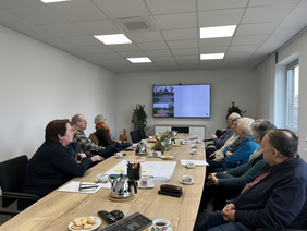 Firma Pro-t-in im Gespräch mit dem Seniorenbeirat an einem Tisch mit Blick auf eine Leinwand.