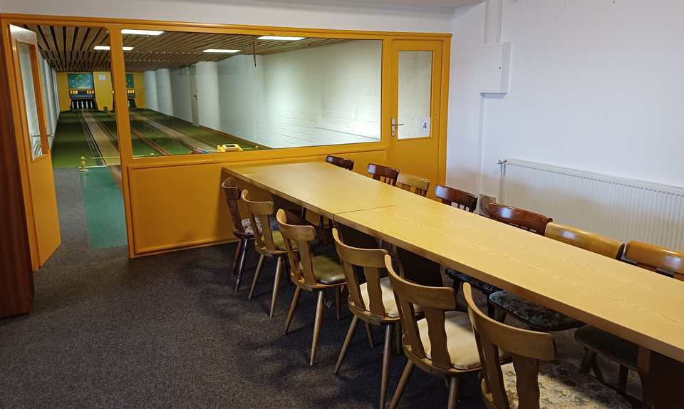 Kegelbahn im Vordergrund Tische mit Stühlen in einer Reihe