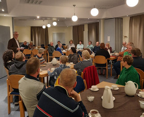 Bürger sitzen an Tischen und hören dem Vortrag des Bürgermeisters zu.