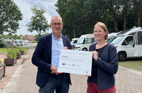 Daniela Kirschsstein, Regionalmanagerin LEADER-Region Fehngebiet, übergibt symbolisch den Bewilligungsbescheid an Bürgermeister Günter Harders