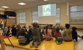 Eine Gruppe Kinder sitzt auf gelben Matten und schaut einen Film