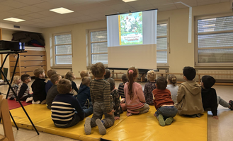 Eine Gruppe Kinder sitzt auf gelben Matten und schaut einen Film