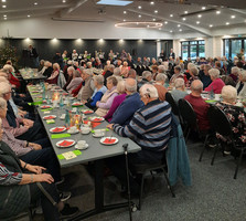 Seniorinnen und Senioren sitzen an der gedeckten Kaffeetafel und hören der Begrüßung des Bürgermeisters zu