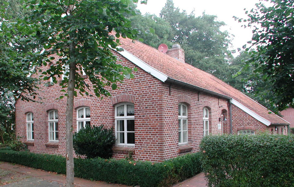 Die alte Schmiede in Potshausen ist ein Fehnhaus. Vor dem Haus stehen Bäume und eine Hecke.