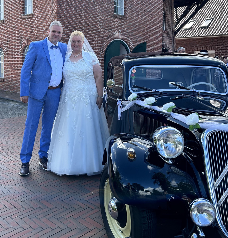 Ein Brautpaar steht neben einem Oldtimer an der Mühle Idafehn