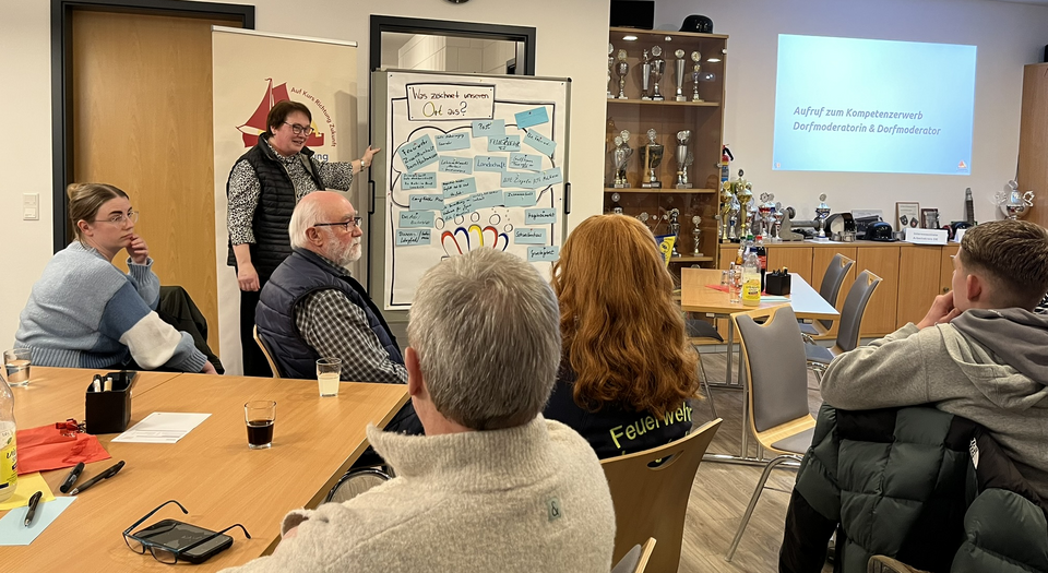 Einwohner sitzen an Gruppentischen und schauen eine Präsentation an