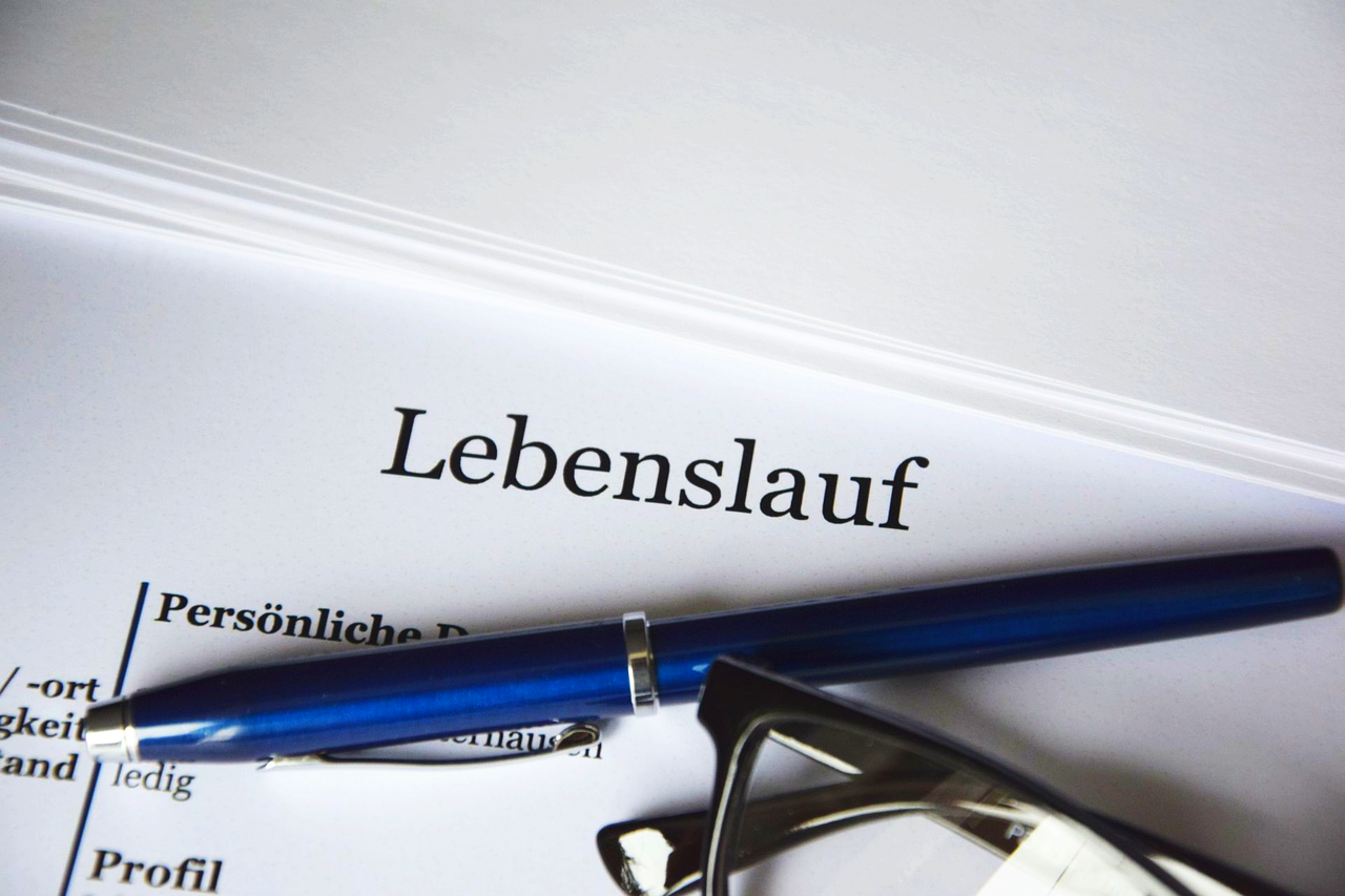 Ein Lebenslauf auf dem ein blauer Stift und eine Brille liegen